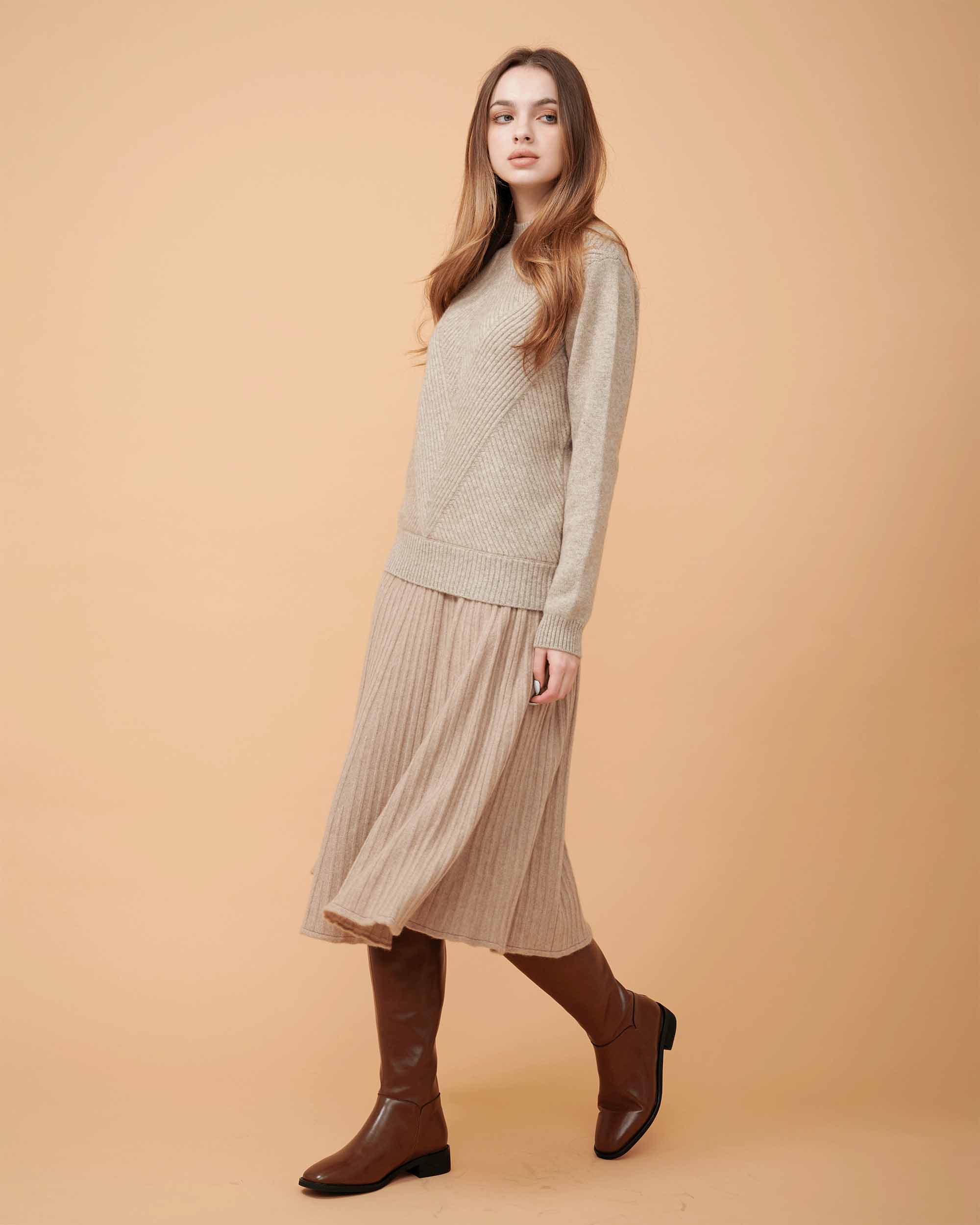 A woman wearing a tan cashmere midi skirt with pleats and a Cashmere sweater