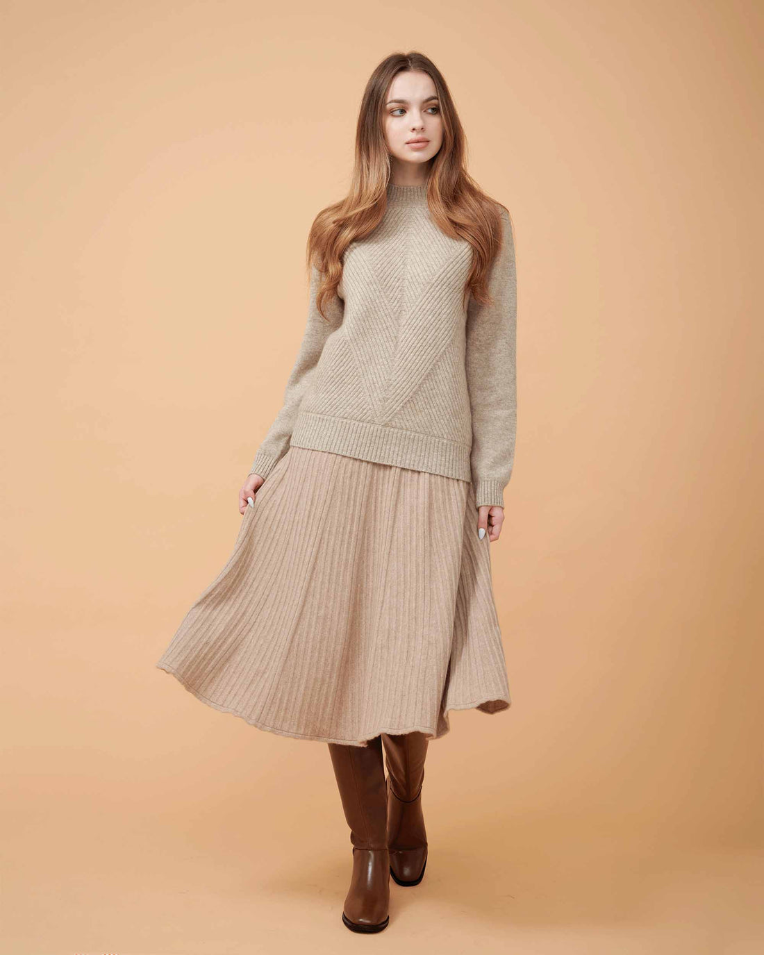 A woman wearing a beige cashmere midi skirt with pleats and a Cashmere sweater