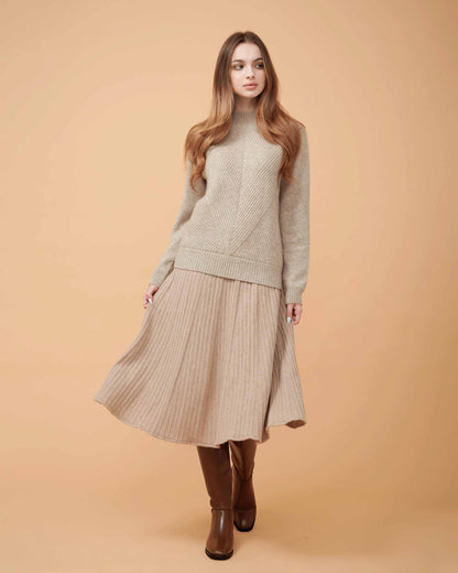 A woman wearing a beige cashmere midi skirt with pleats and a Cashmere sweater