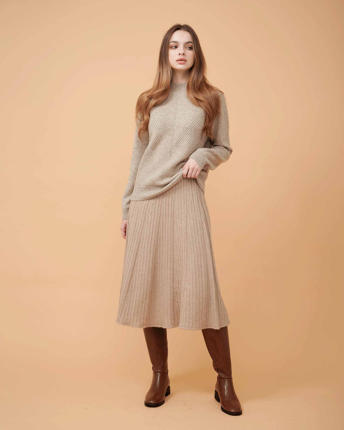 A woman wearing a tan cashmere midi skirt with pleats and a Cashmere sweater