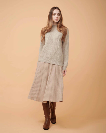 A woman wearing a tan cashmere midi skirt with pleats and a Cashmere sweater
